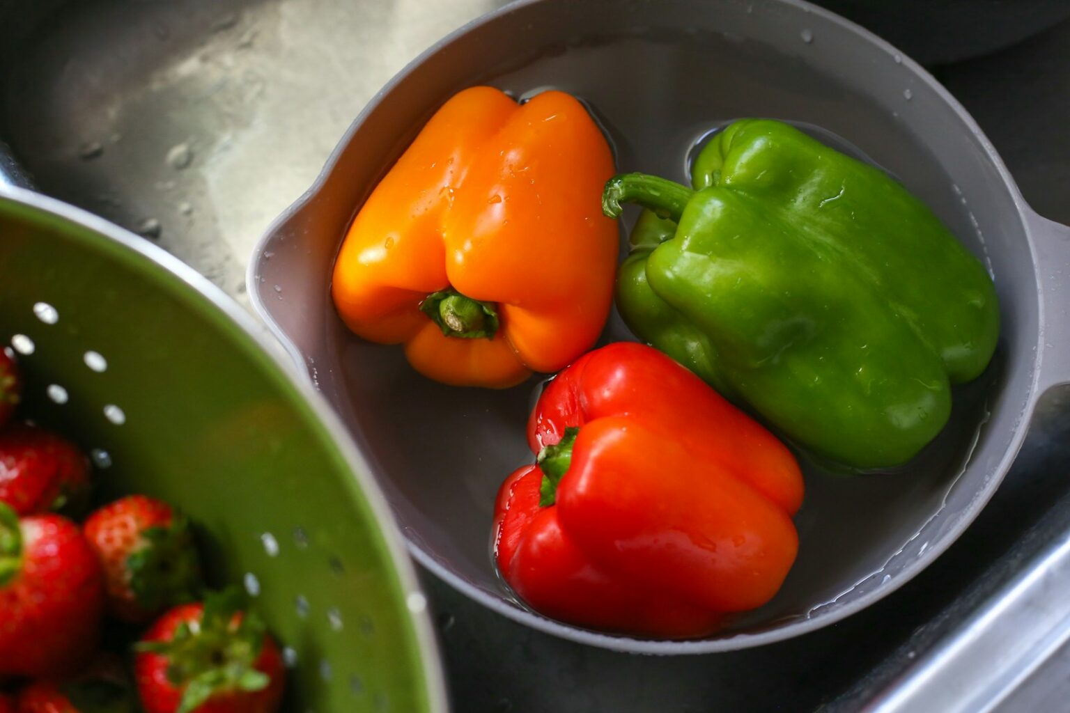 three peppers in a bowl next to a bowl of strawberries