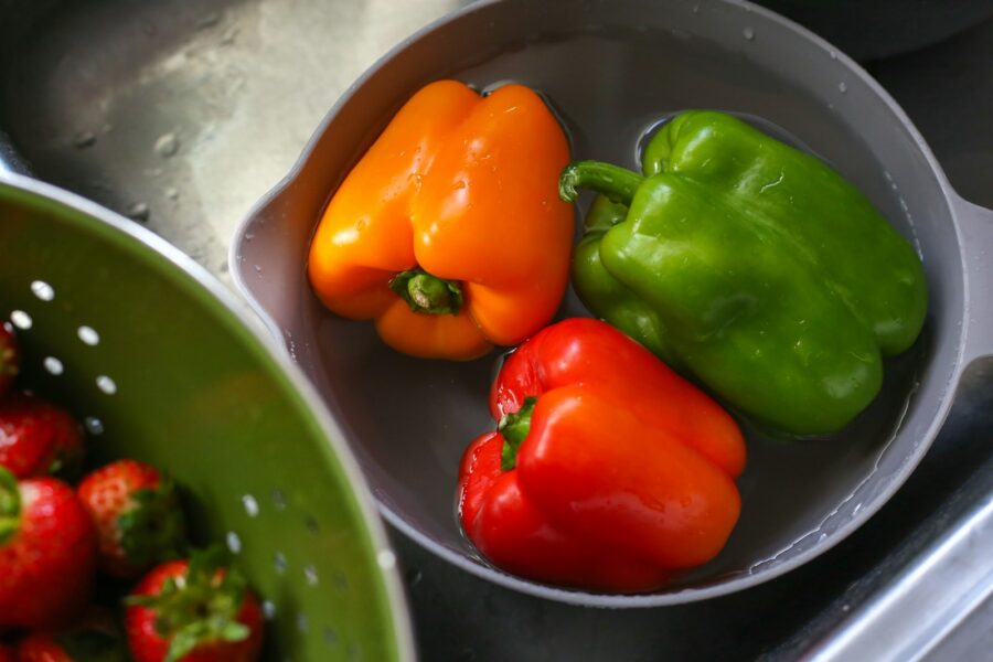 three peppers in a bowl next to a bowl of strawberries