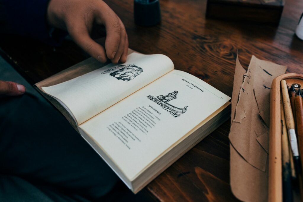 a person holding an open book on top of a wooden table